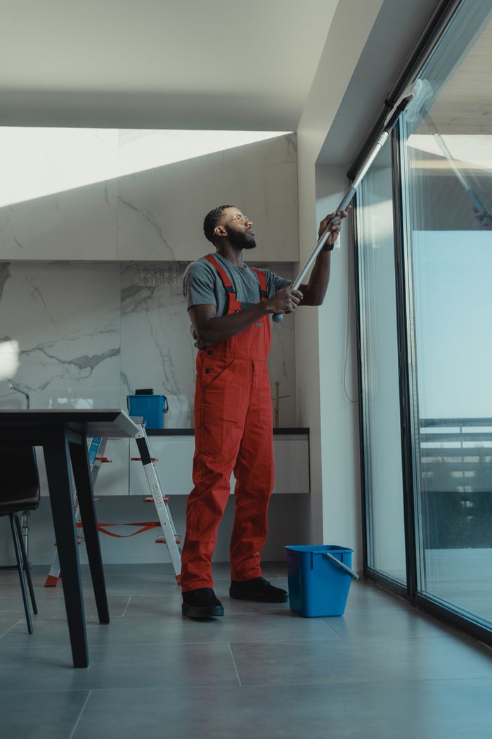 creative-01 A man in coveralls cleans a large window in a stylish, modern home interior.